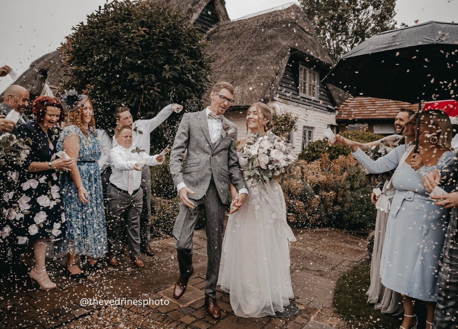 Real wedding confetti photo - Our petals in action - The Dried Petal Company - Wedding couple with confetti, surrounded by guests. Photo credit @thevedrinesphoto