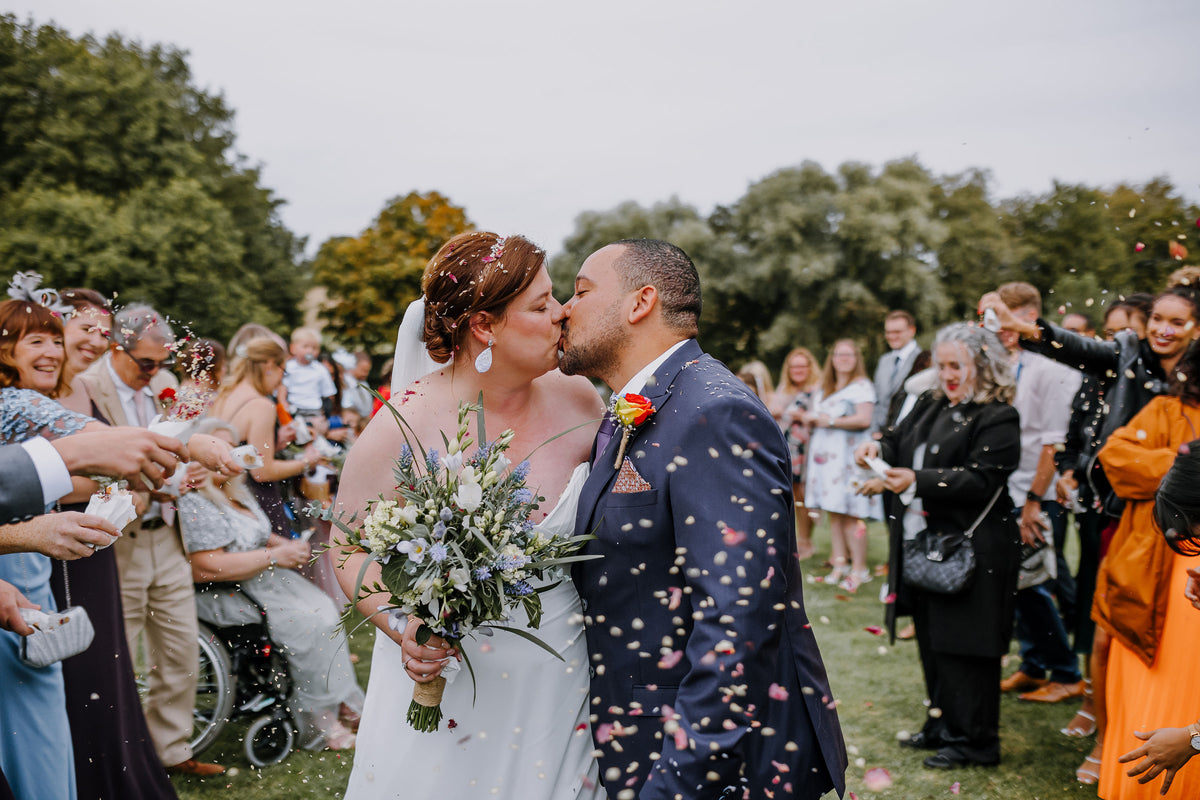 Real wedding confetti photo - Our petals in action - The Dried Petal Company - Wedding couple with confetti, surrounded by guests. Photo credit @ConstanceDoylePhotography